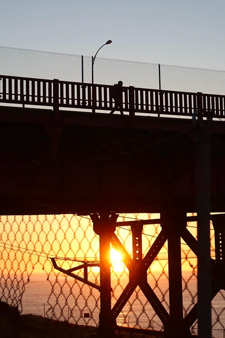 A person walking across a bridge at sunset.